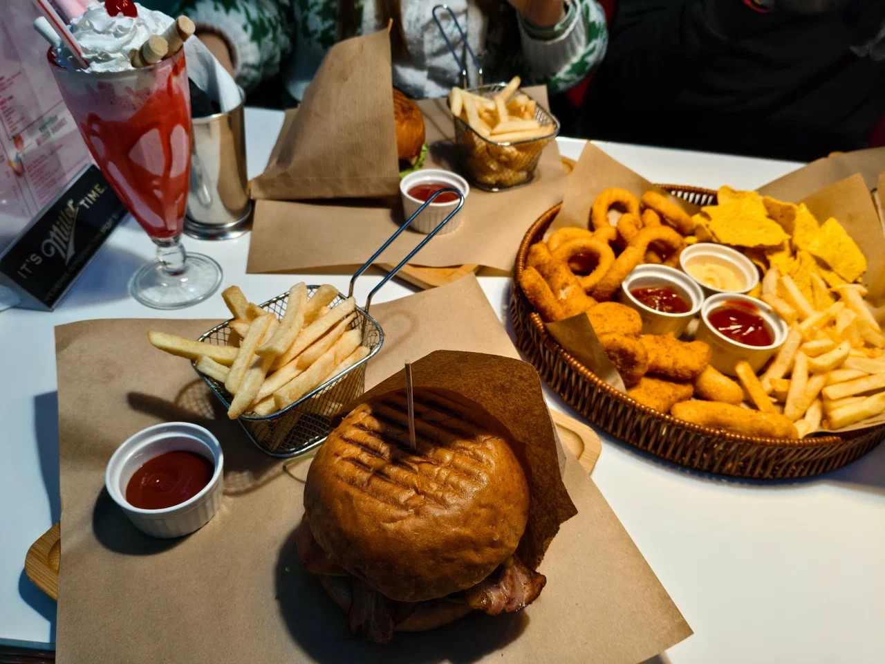 Grilled bacon burger with fries, a strawberry milkshake and a sharing platter of onion rings and nuggets