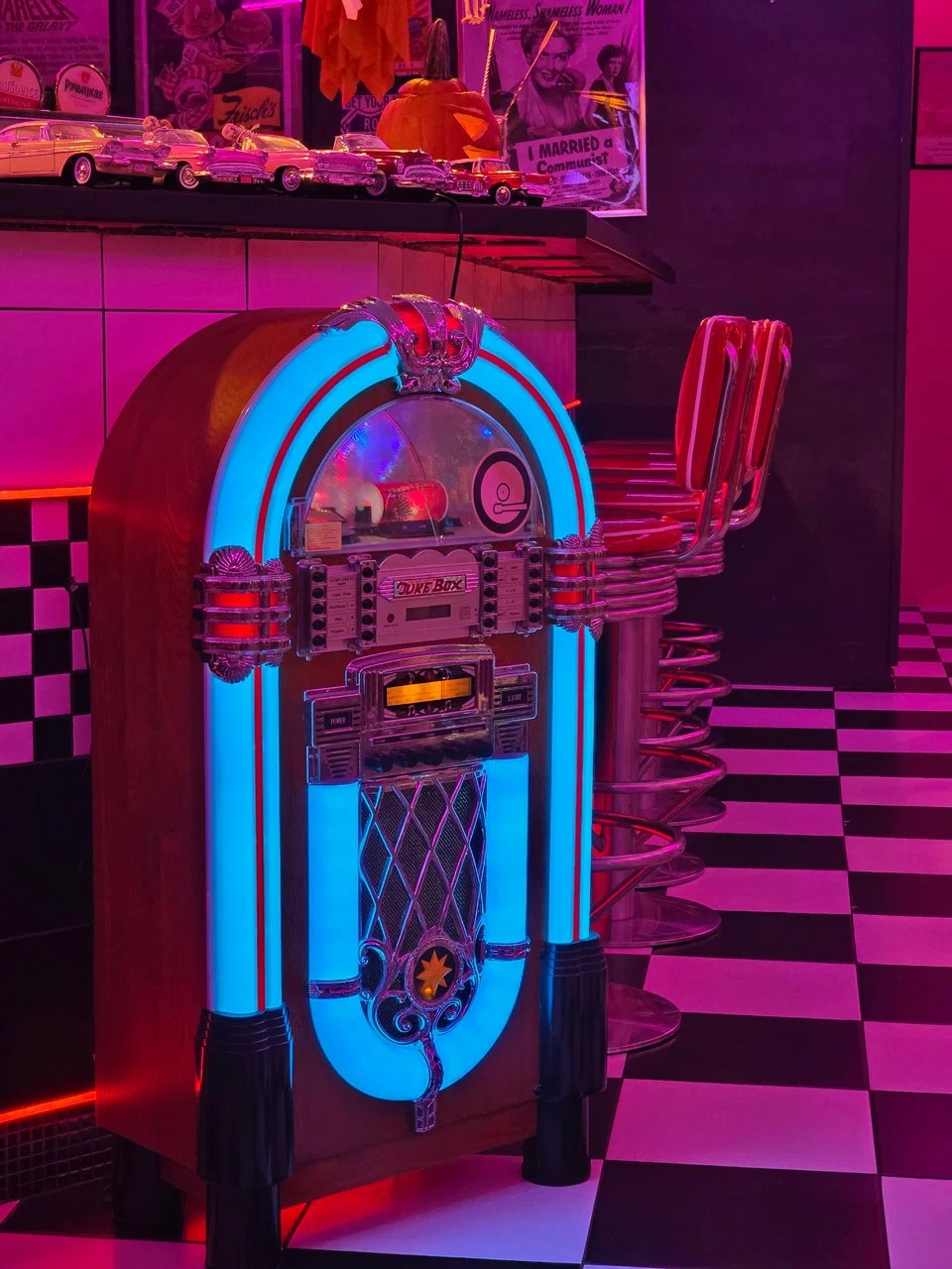 Vintage jukebox glowing turquoise beside red chrome bar stools