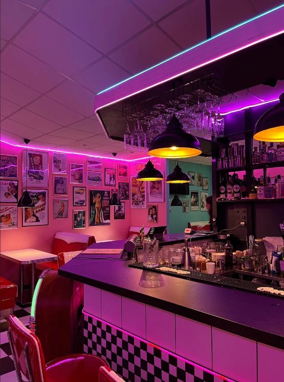 Bar counter glowing in pink and turquoise neon with vintage posters on the wall